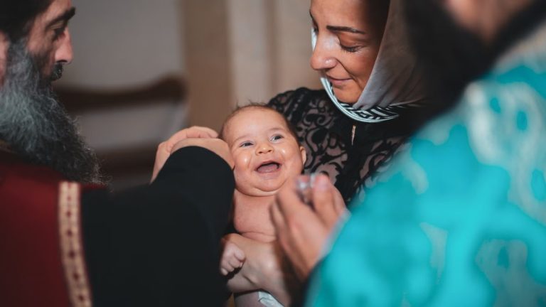 A smiling baby during a baptism ceremony with priest and family in a church.